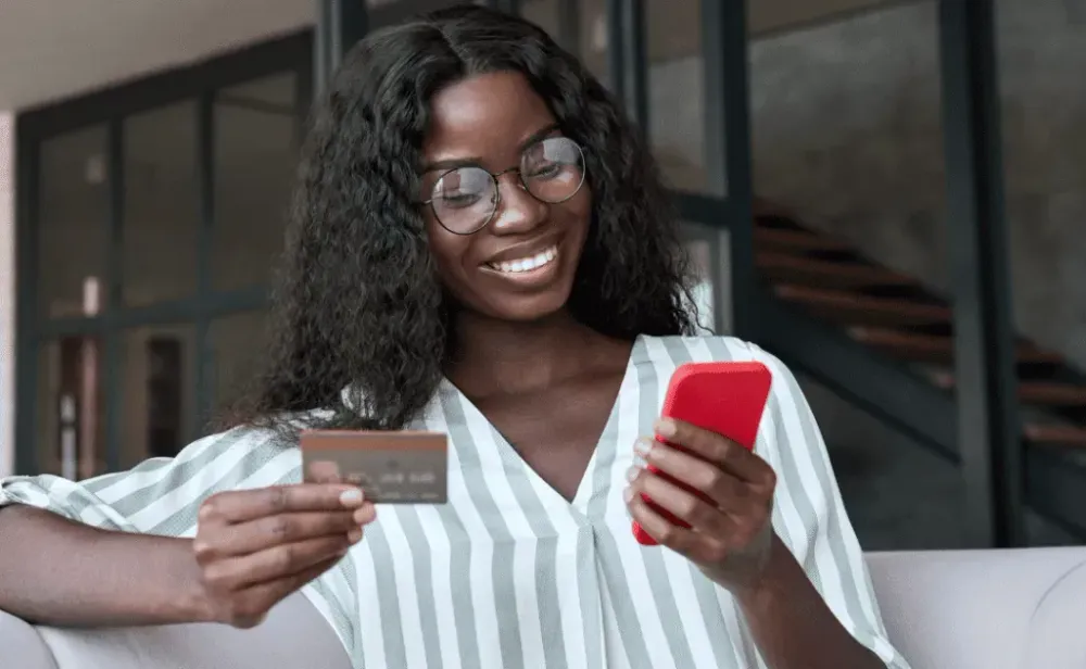 Happy woman holding credit card and cell phone
